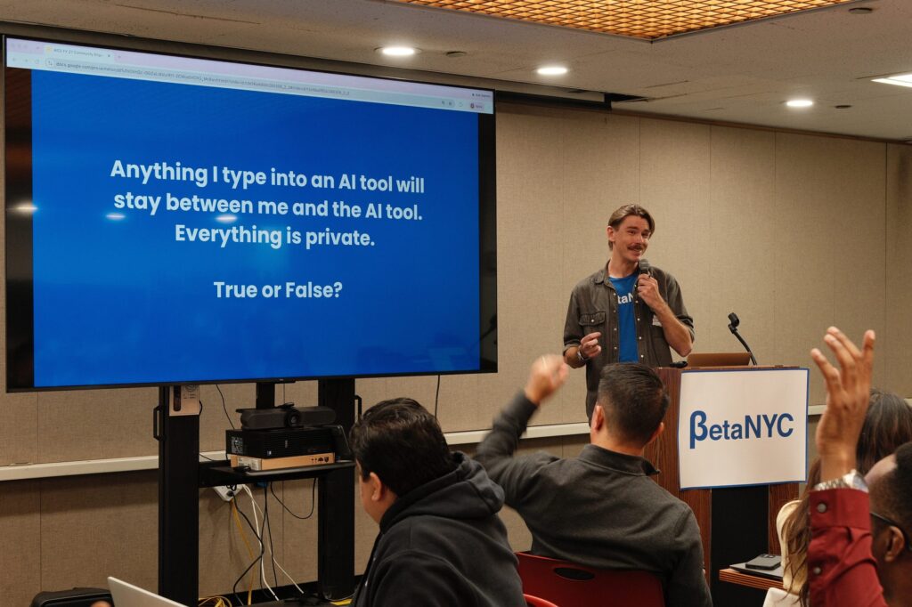 Duncan Ballantine presents beside a slide reading “Anything I type into an AI tool will stay between me and the AI tool. Everything is private. True or False?” as trainers raise their hands.