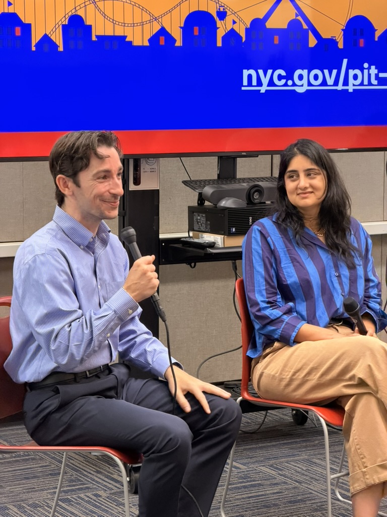 Panelists Luke Farrel and Sukhi Gulati-Gilbert sit with microphones at the BetaBagels event. Luke speaks while Sukhi listens. A presentation screen behind them shows part of the “nyc.gov/pit” link and a city-themed graphic.