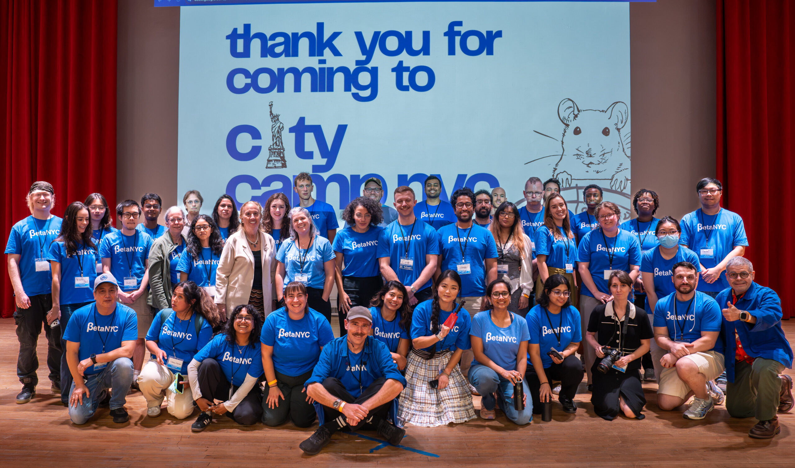 Group photo of CityCamp NYC volunteers in blue BetaNYC shirts on stage, under a "thank you for coming to CityCamp NYC" slide.