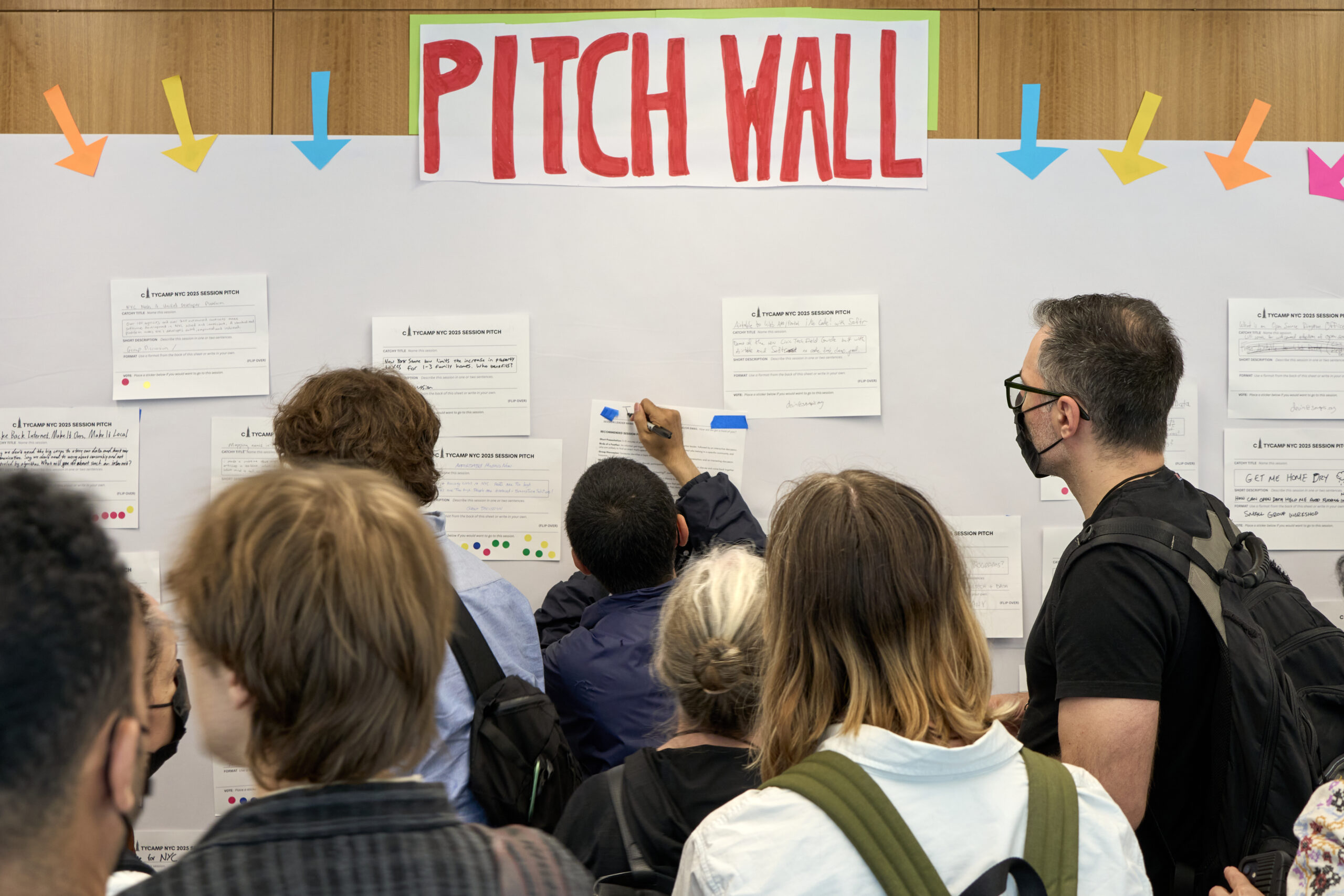 An image of the colorful Pitch Wall where one individual is writing their contact info on their pitch before taping it up among other pitches