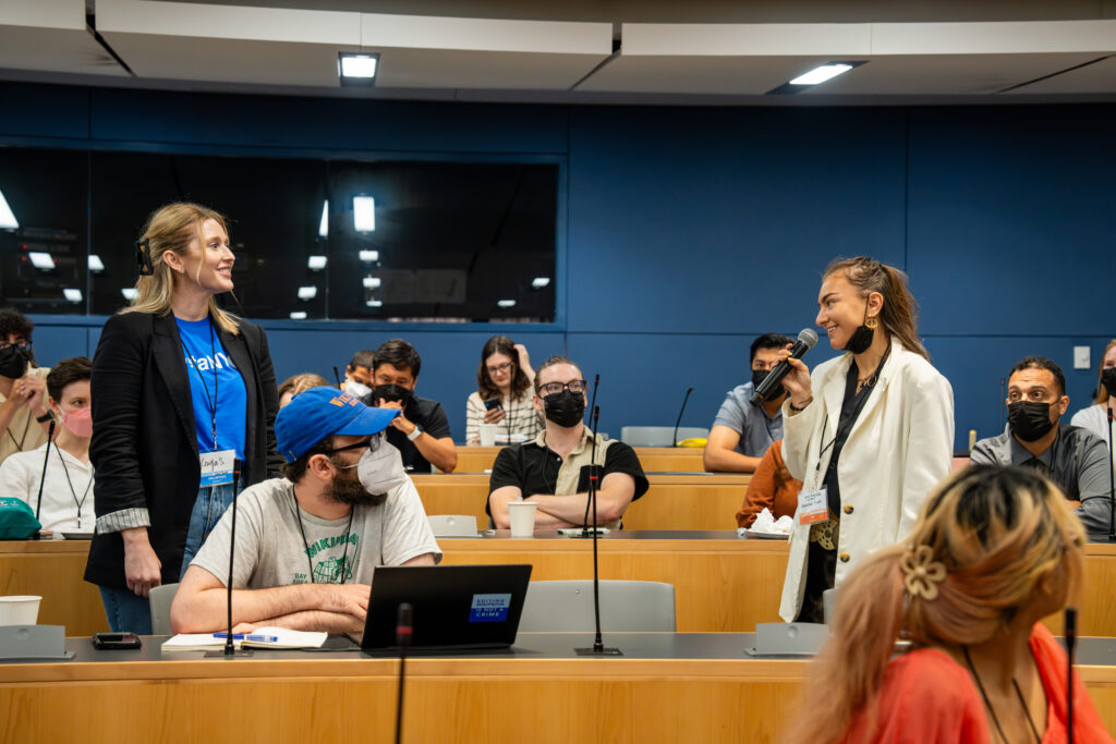 An image of a woman wearing a white blazer pitching a session in an auditorium.