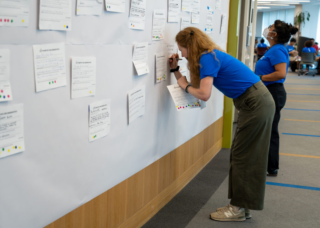 An image of two BetaNYC volunteers wearing bright blue shirts who are examining session pitch cards before moving them to The Board