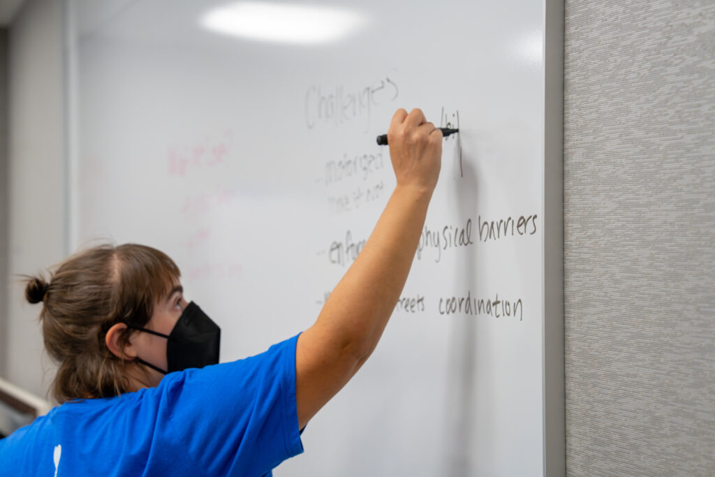 An image of a BetaNYC volunteer writing on a whiteboard in a classroom