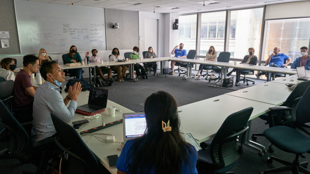 An image of a classroom full of people, seated in a square arrangement where they are all facing each other while discussing a session topic