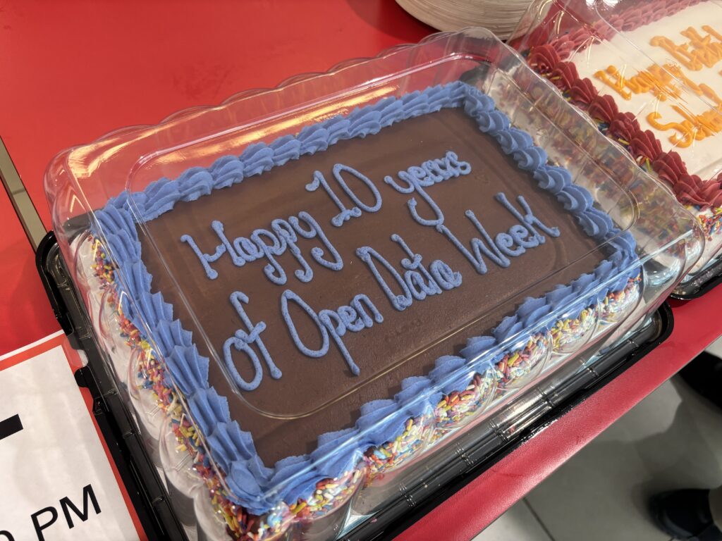 A chocolate sheet cake frosted with the words 'Happy 10 years of Open Data Week' in blue icing, surrounded by colorful sprinkles and a blue border.