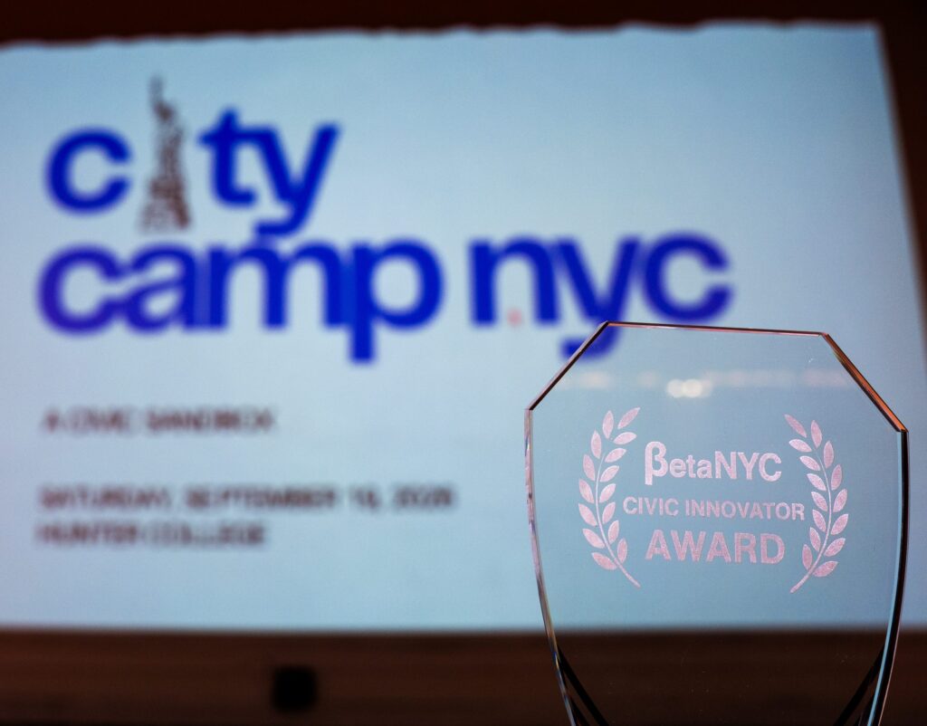 A glass BetaNYC Civic Innovator Award in front of a projected CityCamp NYC title slide.