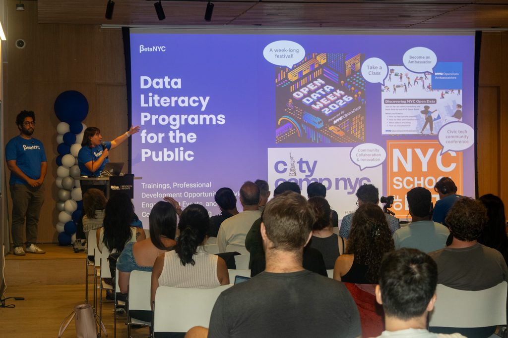 BetaNYC presenters Jordan Shapiro and Sourabh Chakraborty speaking to an audience beside a slide about data literacy programs for the public.
