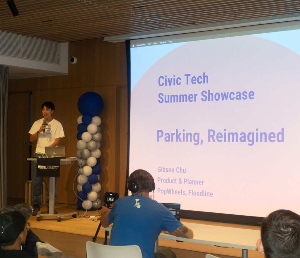 Presenter Gibson Chu at a podium beside a slide titled “Parking, Reimagined” during the Civic Tech Summer Showcase.