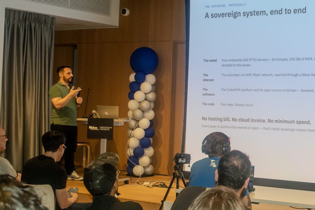 Presenter Matt Keough on stage discussing CodeNOW NYC beside a slide titled “A sovereign system, end to end.”