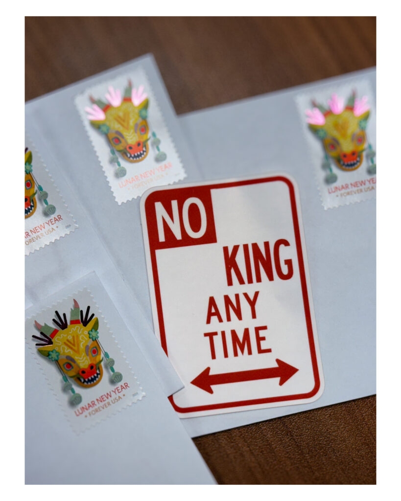 A red and white sticker that reads "NO KING ANY TIME" lies on top of a pile of white envelopes with Lunar New Year postage stamps.
