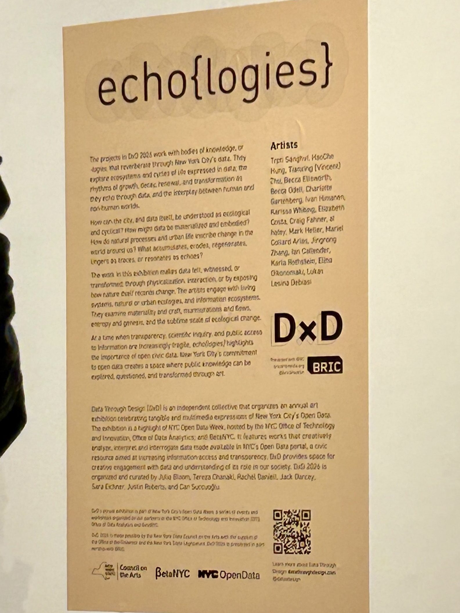 A close-up shot of a tall, beige presentation poster on a gallery wall. The poster's header reads "echo{logies}". The poster explains the exhibition "echo{logies}"
