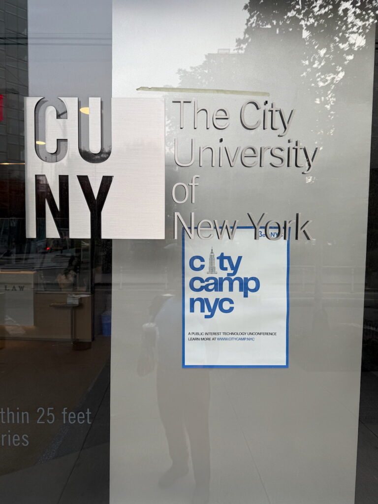 Photo of the CUNY - The City of New York logo with CityCamp NYC poster in the background