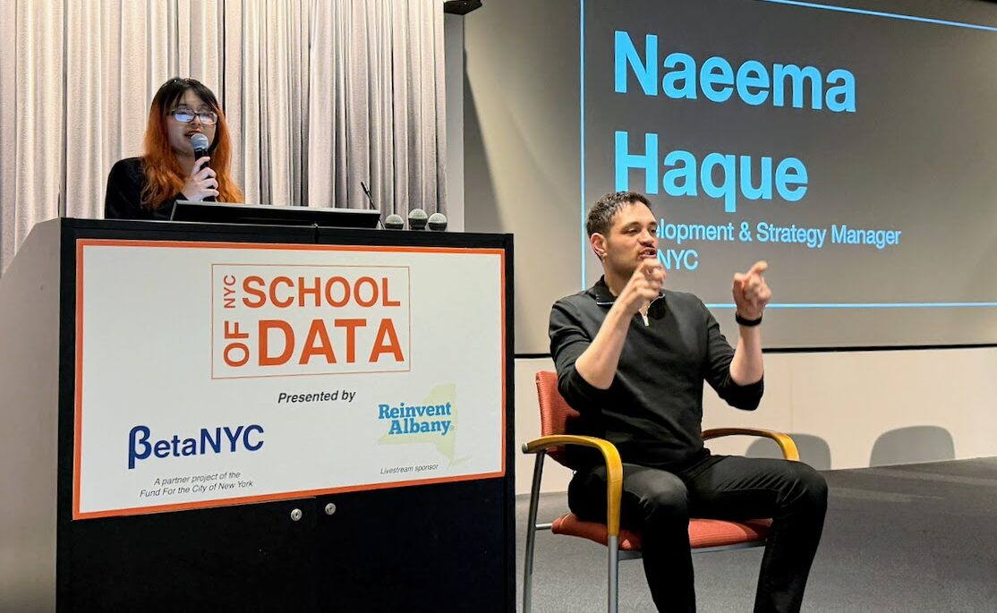 Naeema Haque speaking into a microphone while standing in front of a NYC School of Data lectern