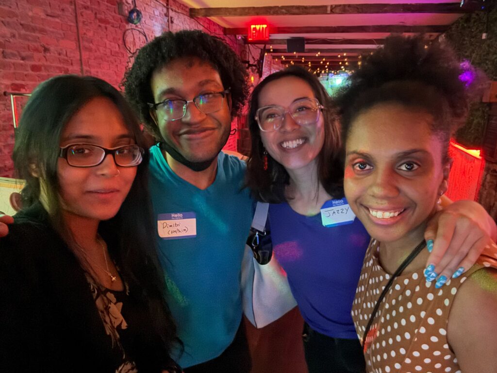 A group of smiling people takes a selfie indoors at a bar/arcade with brick walls.