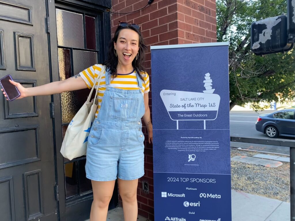 A woman stands outside near black doors and a blue poster that reads: "Entering Salt Lake City State of the Map US The Great Outdoors."