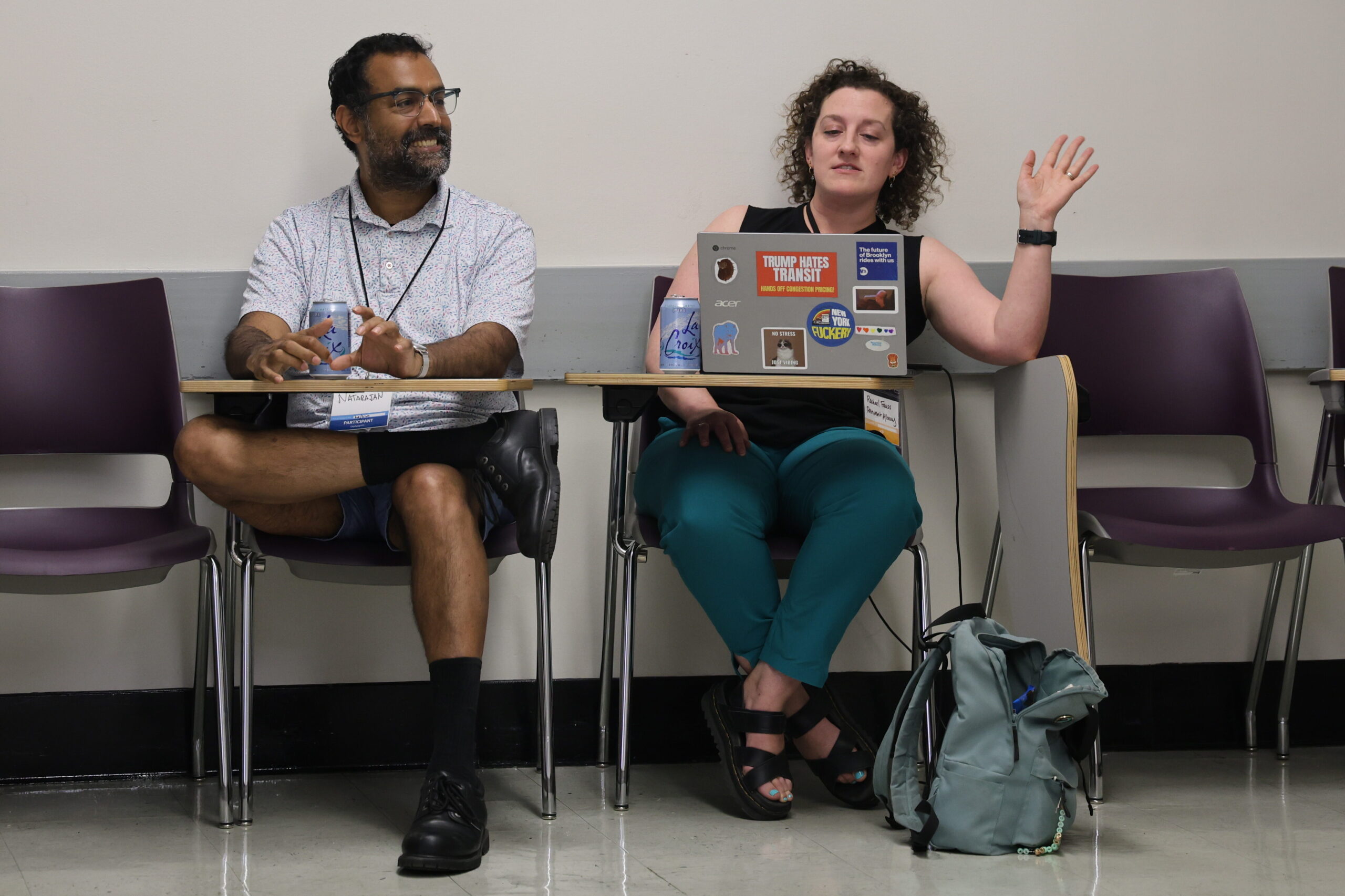 Two participants talk in a breakout session. One raises a hand behind a sticker-covered laptop.