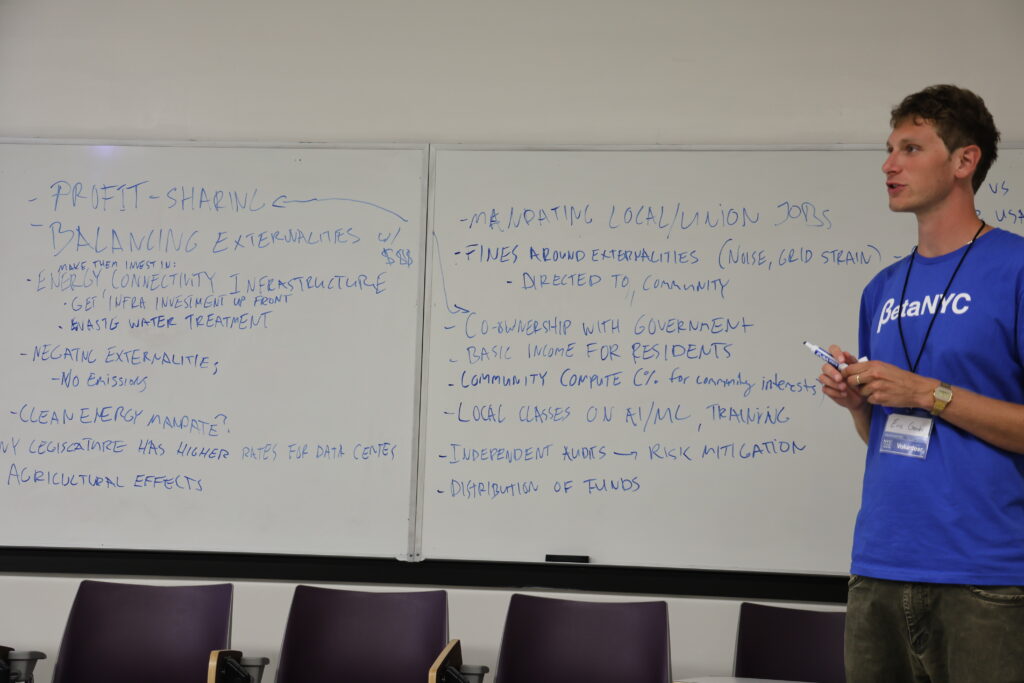 A facilitator in a BetaNYC shirt stands beside whiteboards full of notes on data centers, community benefits, and clean energy.