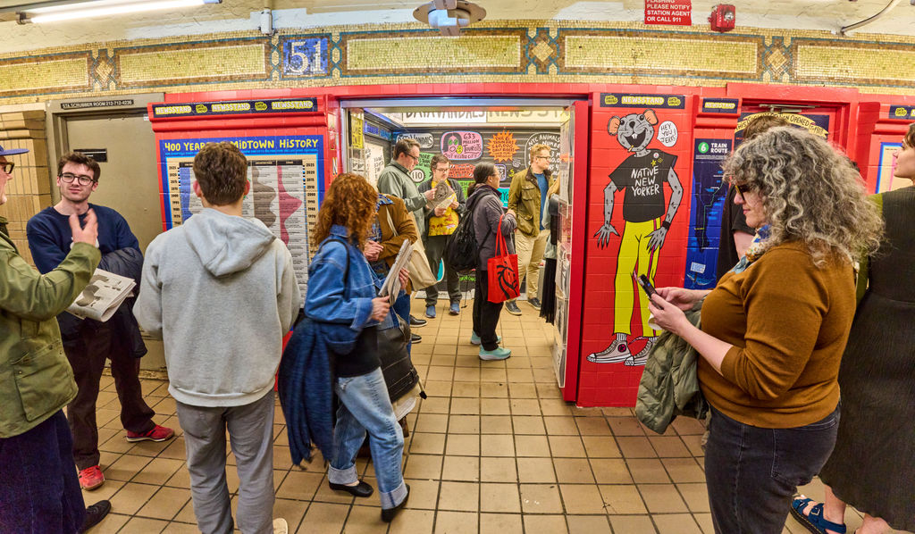 Crowd of commuters in a busy subway station with red lockers and mosaic walls.