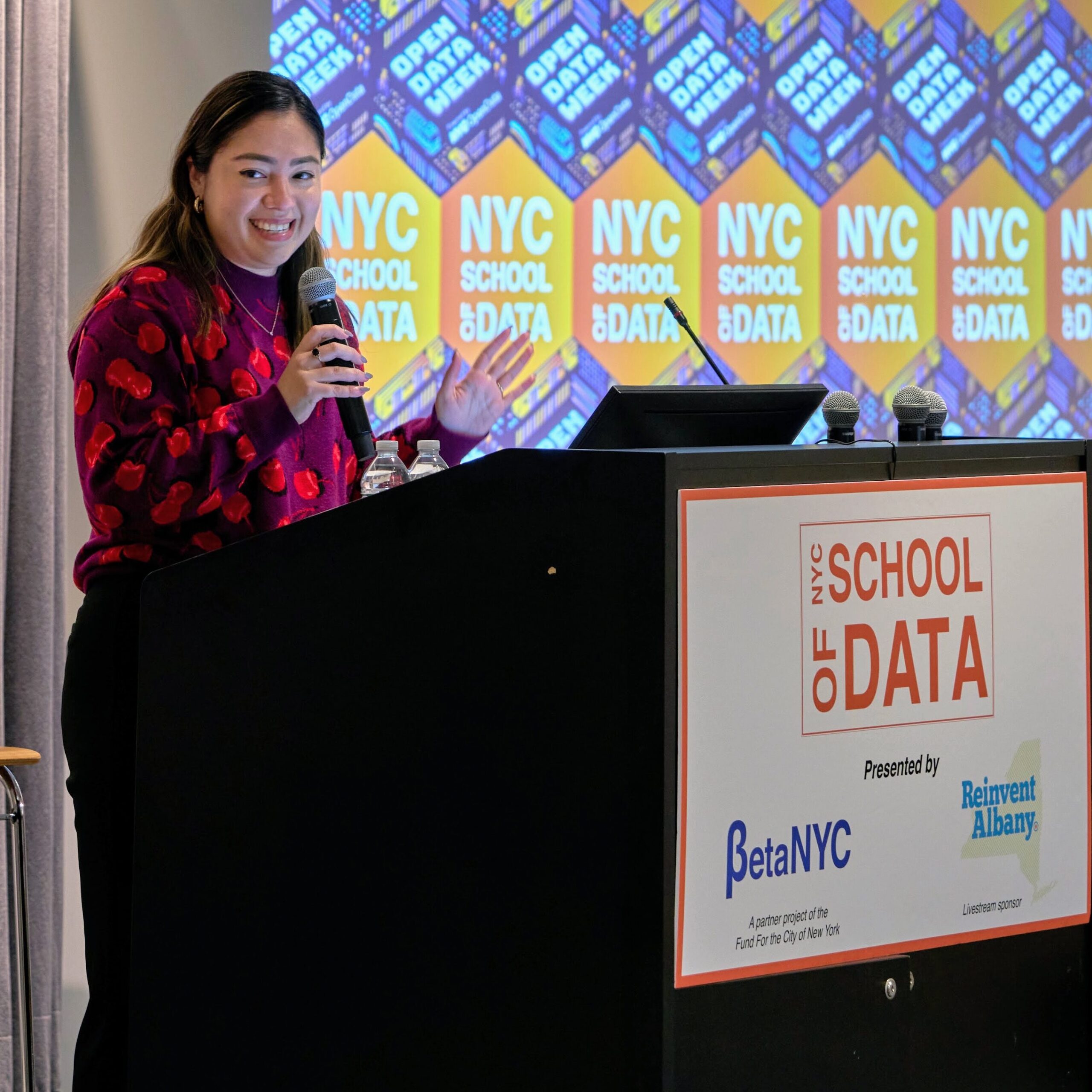 New York State Senator Kristen Gonzalez smiling and speaking into a microphone while standing in front of a NYC School of Data lectern